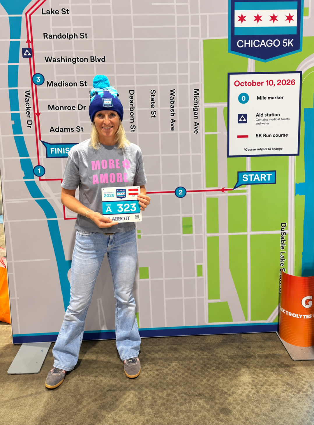 Karin trägt das MORE AMORE Vintage Blue Cropped T-Shirt mit pinkem Frontprint vor dem Chicago-5K-Schild.