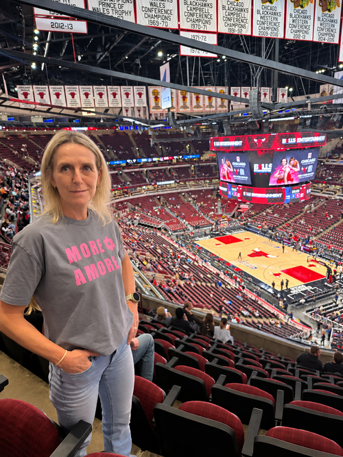 Karin trägt das MORE AMORE Vintage Blue Cropped T-Shirt mit pinkem Frontprint in der Basketballarena in Chicago.
